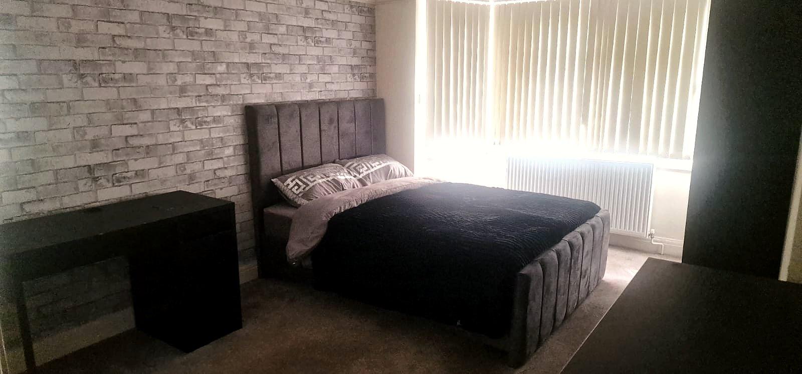 A furnished bedroom with feature wall, desk and double bed
